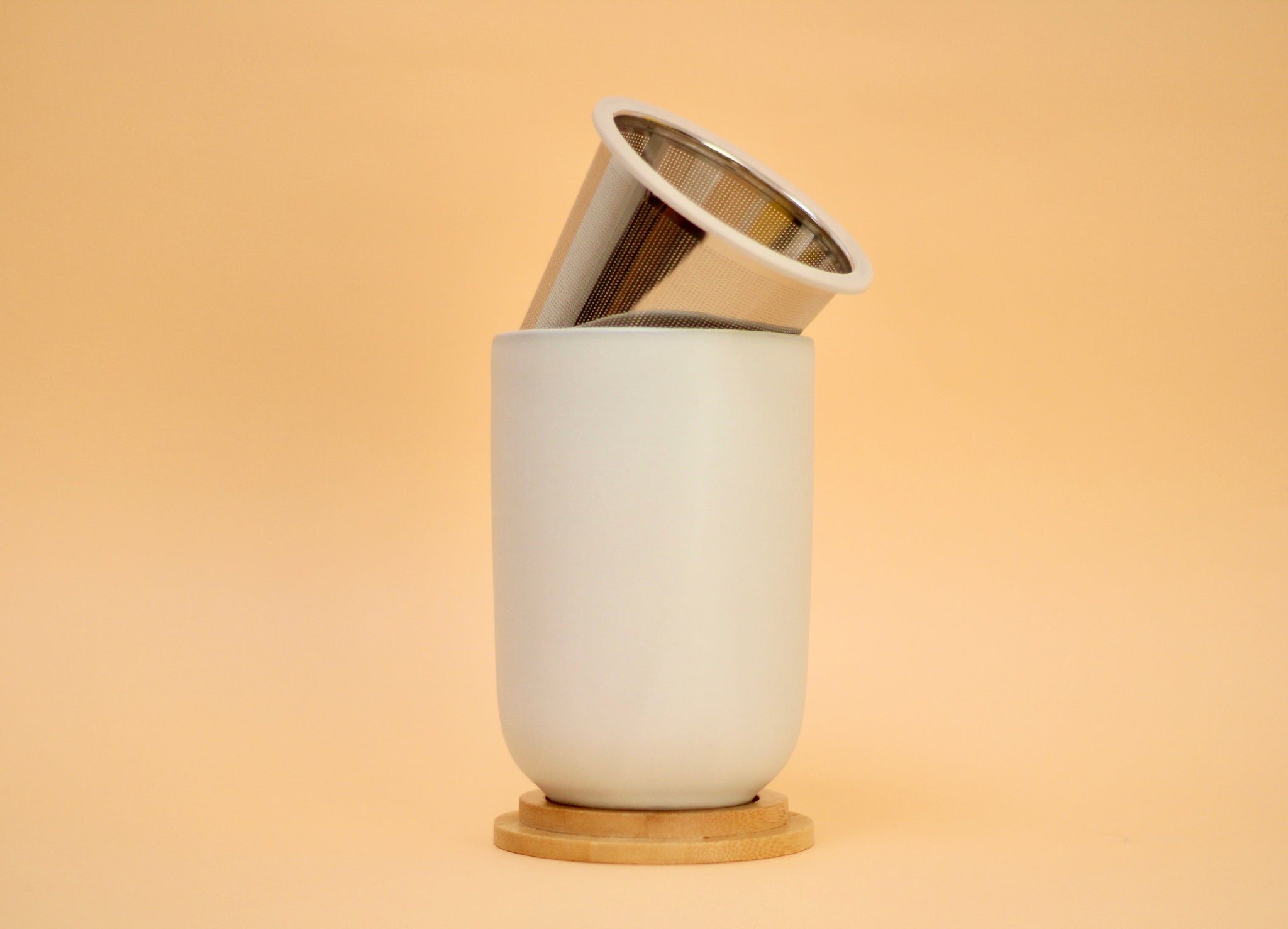White ceramic cup with an infuser and a bamboo lid on a beige background