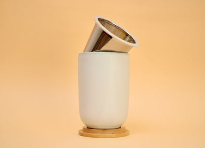 White ceramic cup with an infuser and a bamboo lid on a beige background
